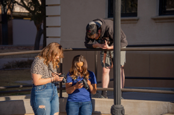 Image of two female students and one male student looking at their cameras.